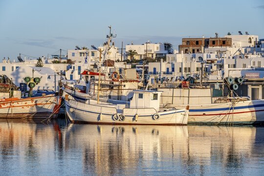 View of Naoussa, Fishing boats in the harbour at sunset, reflected in the sea, White Cycladic houses, Naoussa, Paros, Cyclades, Greece