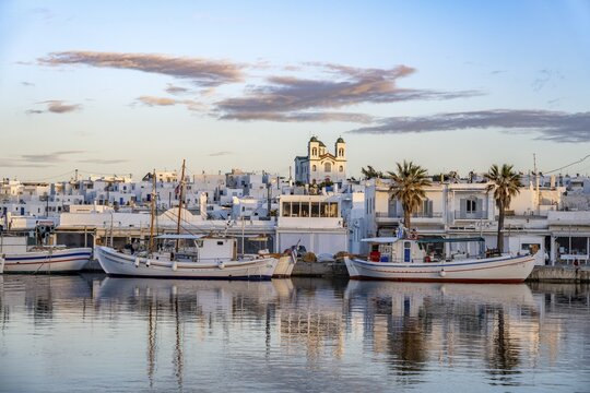 View of Naoussa, Fishing boats in the harbour at sunset, reflected in the sea, White Cycladic houses and church Agios Faneromeni, Naoussa, Paros, Cyclades, Greece