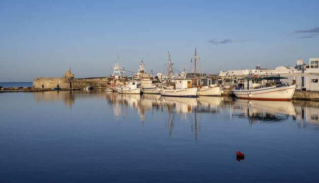 Fishing boats in the harbour and ruins of the Venetian castle, reflected in the sea, at sunset, Naoussa, Paros, Cyclades, Greece