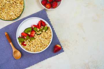 A vibrant bowl of healthy oatmeal topped with fresh sliced kiwi and strawberries sits beside a wooden spoon, promising a nutritious start.
