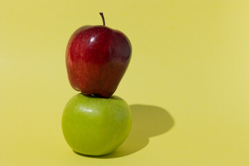 red apple on green apple stacked and isolated on a yellow background with space for text concept of...