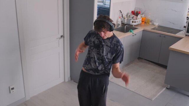 A brunette man in a black printed T-shirt and headphones dances in a m
