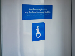 Blue passenger priority sign with wheelchair symbol and bilingual text, indicating reserved area for people with disabilities in public transportation, promoting accessibility.