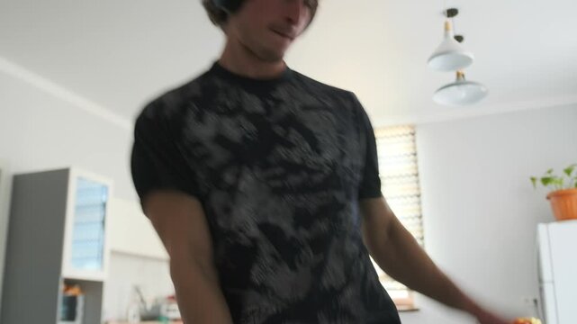 A young man in a black T-shirt and headphones dances in a modern kitch