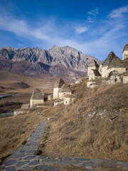 Fototapeta premium Ancient stone structures on a hillside, surrounded by rugged mountains and clear blue sky, showcasing historical architecture and natural beauty in a serene landscape