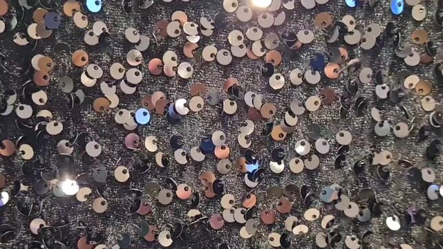 Moving background of black sequin fabric surface with multicolored sequins for decoration. Surface of rough velvet fabric with small metallic sequins gives a shimmering effect when exposed to light.