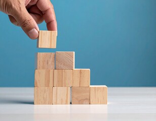 Hand placing wooden block onto a pyramid stack against a blue background
