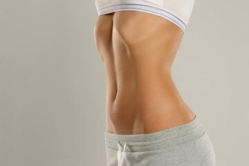 Side view of a woman&rsquo;s torso with toned abdomen and slim waist, studio shot on a gray background