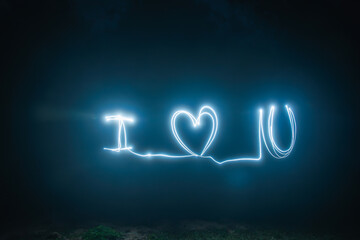 Creative light painting photography of "I Love You" text and heart symbol against a dark night background, perfect for Valentine's Day or romantic concepts.