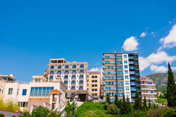 Residential buildings on a hillside under a bright blue sky in Montenegro. Urban development, tourism growth, and modern coastal living shaped by architecture and natural landscape.