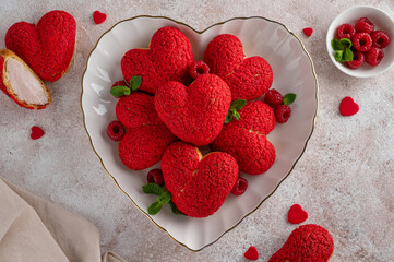 Heart-shaped profiteroles with red craquelin and raspberry cream - Valentine's Day dessert on a plate on a concrete background. Top view, copy space.
