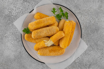 Crispy breaded mozzarella sticks on a plate with parsley, served with ketchup and mustard dips. Golden fried texture, appetizing snack on gray background