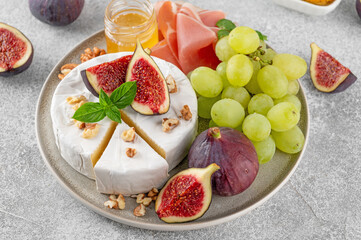 Camembert, bree cheese, walnuts, fresh figs, grapes, prosciutto and honey on a plate on a concrete background. Charcuterie plate. Top view