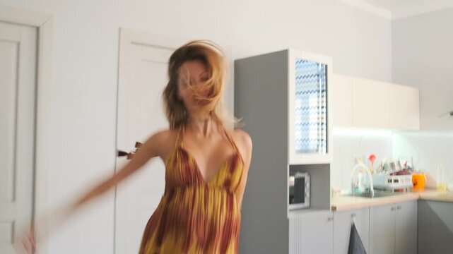A young woman in an orange tie-dye sundress dances and jumps in the ki