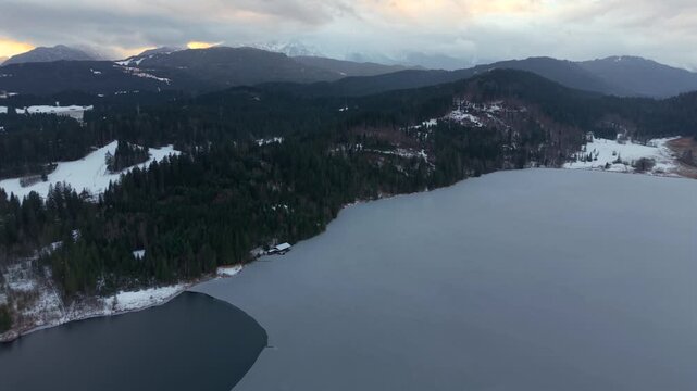 Aerial video of Barmsee, an alpine lake in Oberbayern, Germany. Winter conditions with frozen water, forest and mountain backdrop by drone. Winter aerial landscape with frozen lake and Karwendel Alps