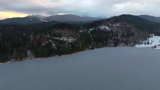 Aerial winter panorama of Barmsee in Oberbayern. Drone video shows calm alpine lake, partial ice cover and mountain backdrop. Spectacular panoramic view of Bavarian nature in the cold season.