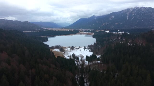 Drone footage above Barmsee in Oberbayern, Germany. Frozen winter lake near Kruen and Wallgau with mountain backdrop of the Karwendel Alps, captured from the air in calm winter conditions.