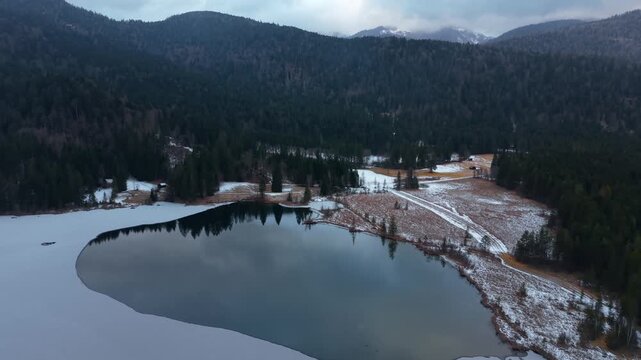 Aerial panorama of the Karwendel mountains backdrop over Barmsee. Aerial view of winter landscape at Barmsee in Bavaria. Frozen alpine lake near Mittenwald captured in cinematic drone footage