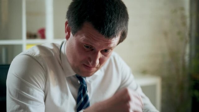Handheld portrait shot of a tired office worker reviewing documents at desk. Man removes glasses and rubs eyes from fatigue, then continues working, showing stress, workload