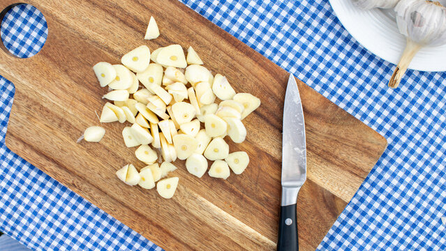 Sliced garlic on rustic board, culinary alchemy for Stinking Rose Festival, vampiric warding, aromatic kitchen odyssey