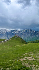 Fototapeta premium Majestic snow-capped peaks cradle ancient chapel under brooding clouds, echoing Caucasus mythology and serene Mountain Day introspection