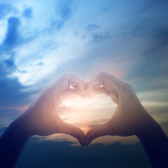 Two hands making a heart shape gesture against a beautiful sunset sky. Concept of love, hope, peace, faith, kindness, sharing, care, and support