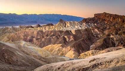 Eroded desert landscape with layered rock formations under a colorful sunrise/sunset sky