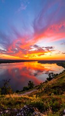 Vibrant sunset reflected in a wide river, seen from a grassy hill