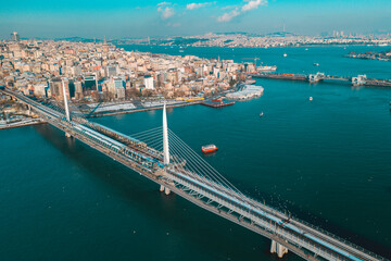 Obraz premium The Golden Horn Metro Bridge and Galata Bridge rise above the blue waters as ships move through the channel in a broad Istanbul landscape.