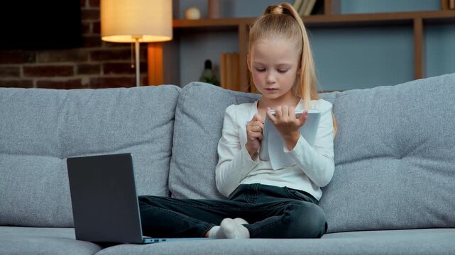 Caucasian child kid pupil girl writing homework at copybook at home schoolgirl focused write preparing to exams with laptop e-learning elementary school learning daughter studying online education