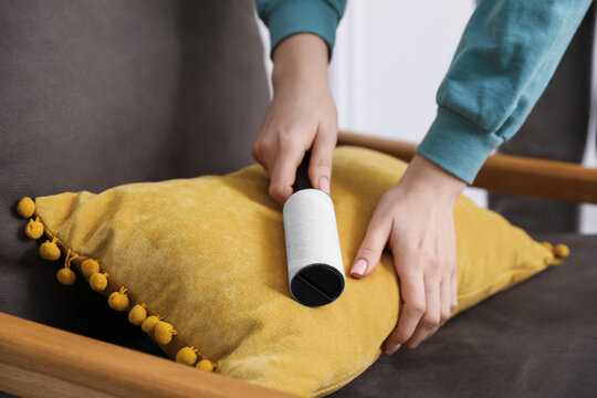 Woman cleaning pillow with lint roller at home, closeup