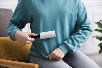 Woman cleaning sweatshirt with lint roller at home, closeup