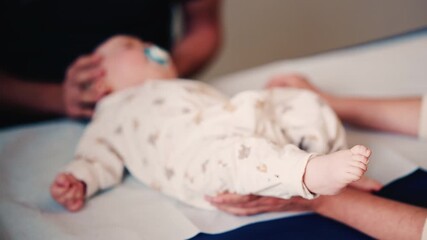 Close up of an adult gently holding a baby's hand while another caregiver supports the infant's head during a medical or wellness check