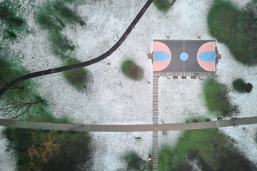 Drone view of outdoor basketball court and park covered in snow