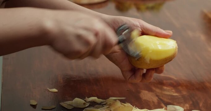 Close up of hands peeling fresh potato with peeler on wooden table, preparing ingredients for homemade vegan meal, cooking process, healthy food, rustic kitchen atmosphere, natural lifestyle