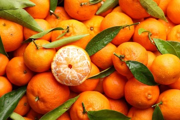 Many fresh ripe tangerines with green leaves and water drops as background, top view