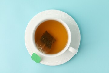 Tea brewing. Cup with tea bag on light blue background, top view