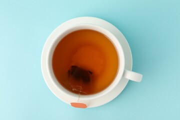 Tea brewing. Cup with tea bag on light blue background, top view