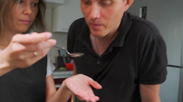 A couple prepares a dish the woman takes a spoon of hot vegetable brot