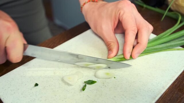 Male hands finely slice fresh green onions on a cutting board and plac