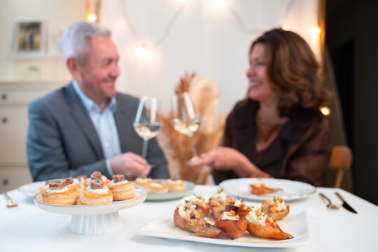 Gourmet appetizers in foreground with mature couple toasting white wine during an elegant home dinner
