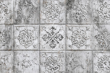 Textured plaster wall with repeating floral relief patterns in muted gray tones