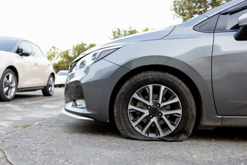Silver car with a flat front tire parked on the street.