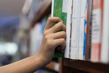 Close up of hand search for book on bookshelves in library. Hand reaching a book on library shelf. Library and book on shelf © amorn