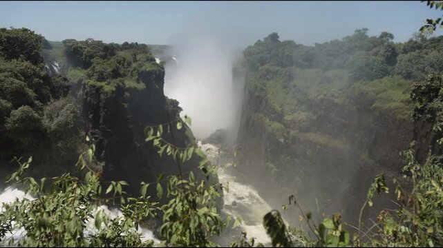 Natural world wonder of Victoria Falls waterfall from Zimbabwe side looking towards giant water fall, rain forest, double rainbow, slow motion, mist, Zambezi River, and plants in beautiful landscape