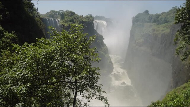 Natural world wonder of Victoria Falls waterfall from Zimbabwe side looking towards giant water fall, rain forest, double rainbow, slow motion, mist, Zambezi River, and plants in beautiful landscape