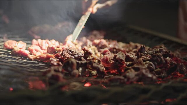 Night time cooking, grilling, and warming fresh goat meat over fire and pot on grill top grate in Africa with Zimbabwe culture, cooks, and people working together to feast on red meats outdoors