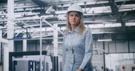 Curly Haired Woman Wearing Protective Helmet Moves Calmly Across High Tech Factory Floor, Observing Robotic Systems and Automated Machinery in Operation. Concept of Digital Manufacturing, Innovation.