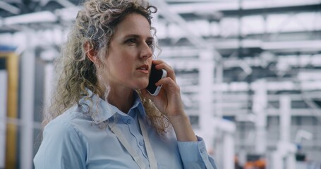 Close up of Female Engineer Talking on Mobile Phone With Serious Expression. Woman Standing in Modern Industrial Plant. Concept of Critical, Real Time Communication and Rapid Response Protocols.