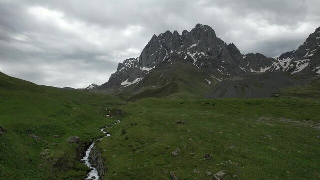 Aerial drone view high above a mountain river near Juta, Georgia, flowing through an alpine valley with rocky terrain and green slopes. Chaukhi Pass area and surrounding Caucasus mountains